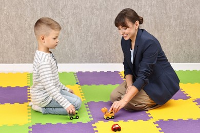 Photo of Autism therapy. Smiling psychologist and little boy playing with toy cars in mental health center