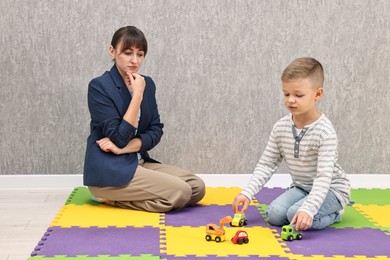 Psychologist observing little boy playing in autism treatment center