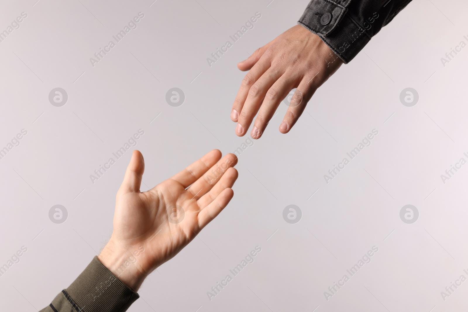 Photo of Man reaching for helping hand on light grey background, closeup