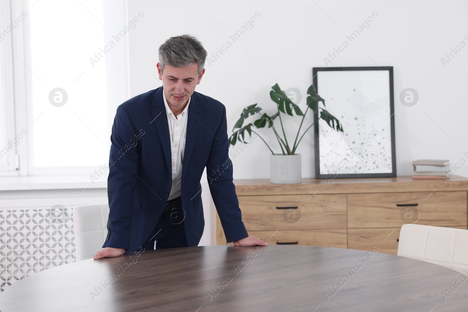 Photo of Man looking at something on desk in office. Space for text