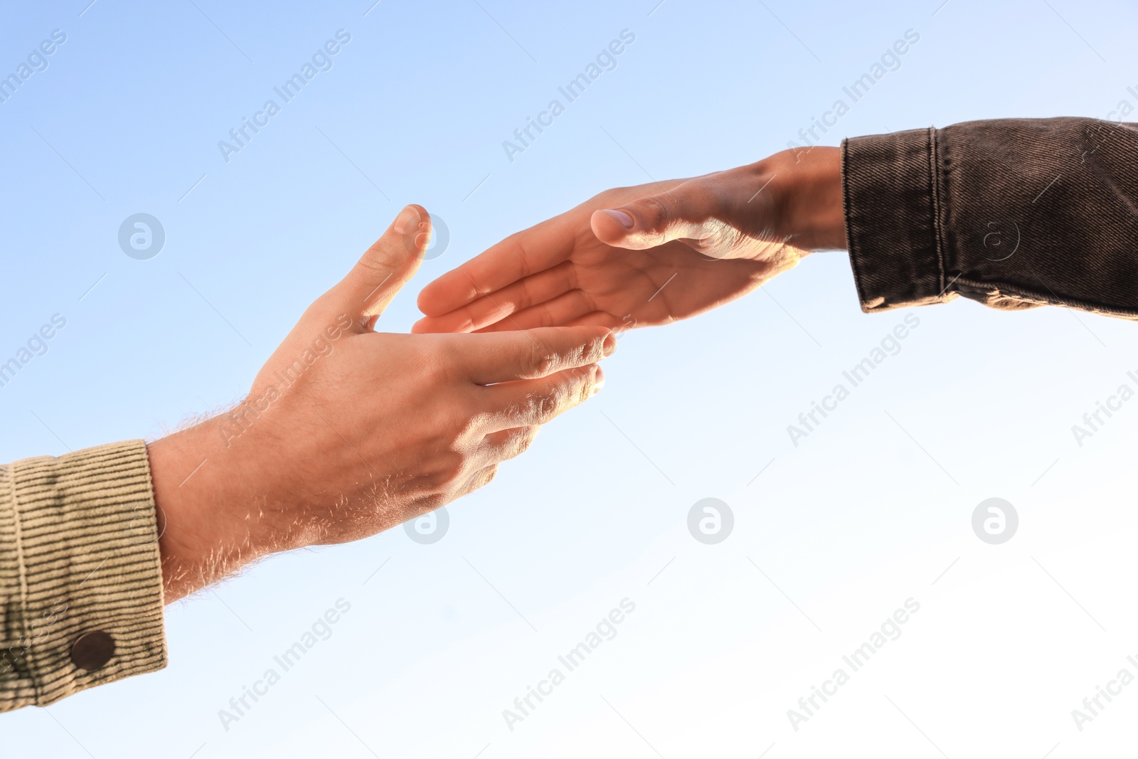 Photo of Man offering helping hand to his friend against blue sky, closeup