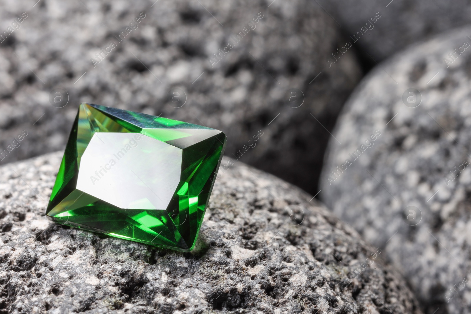 Photo of Beautiful shiny green gemstone on stone, closeup. Space for text