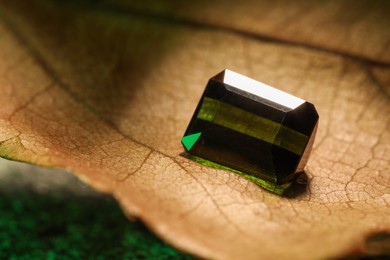 Photo of Shiny green gemstone on dry leaf, closeup