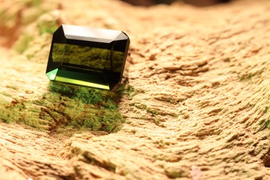 Photo of Beautiful shiny green gemstone on stone, space for text