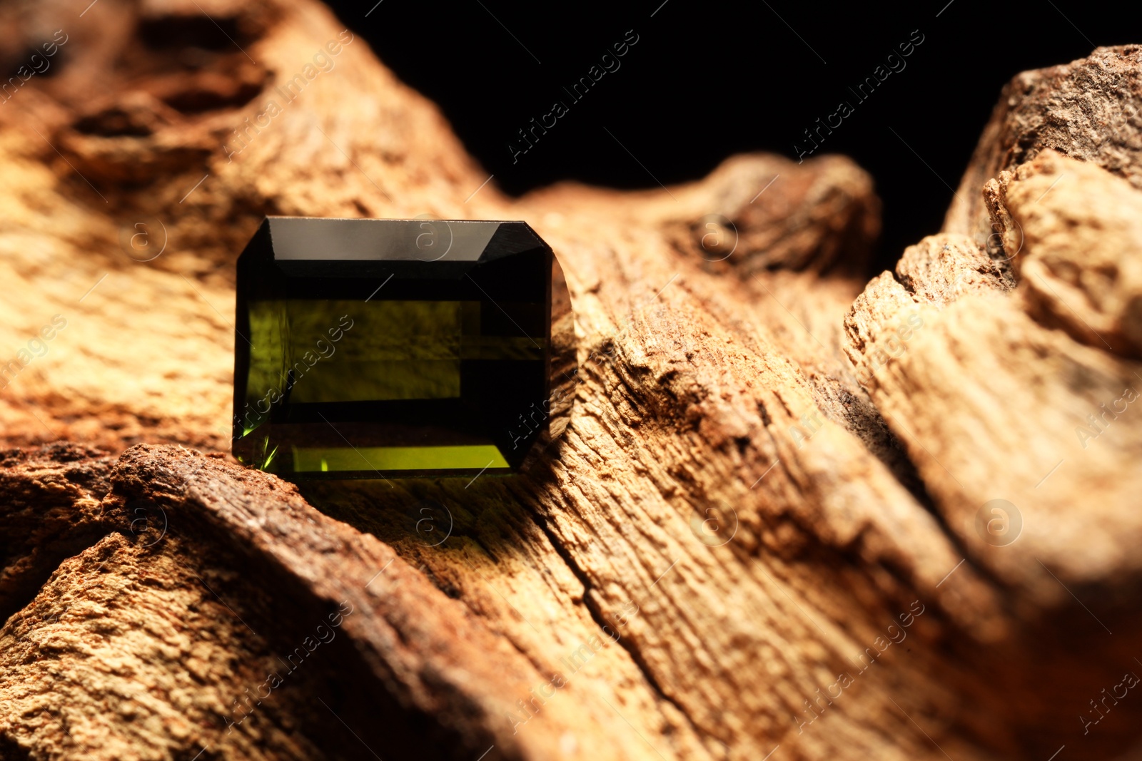 Photo of Beautiful shiny green gemstone on stone against dark background