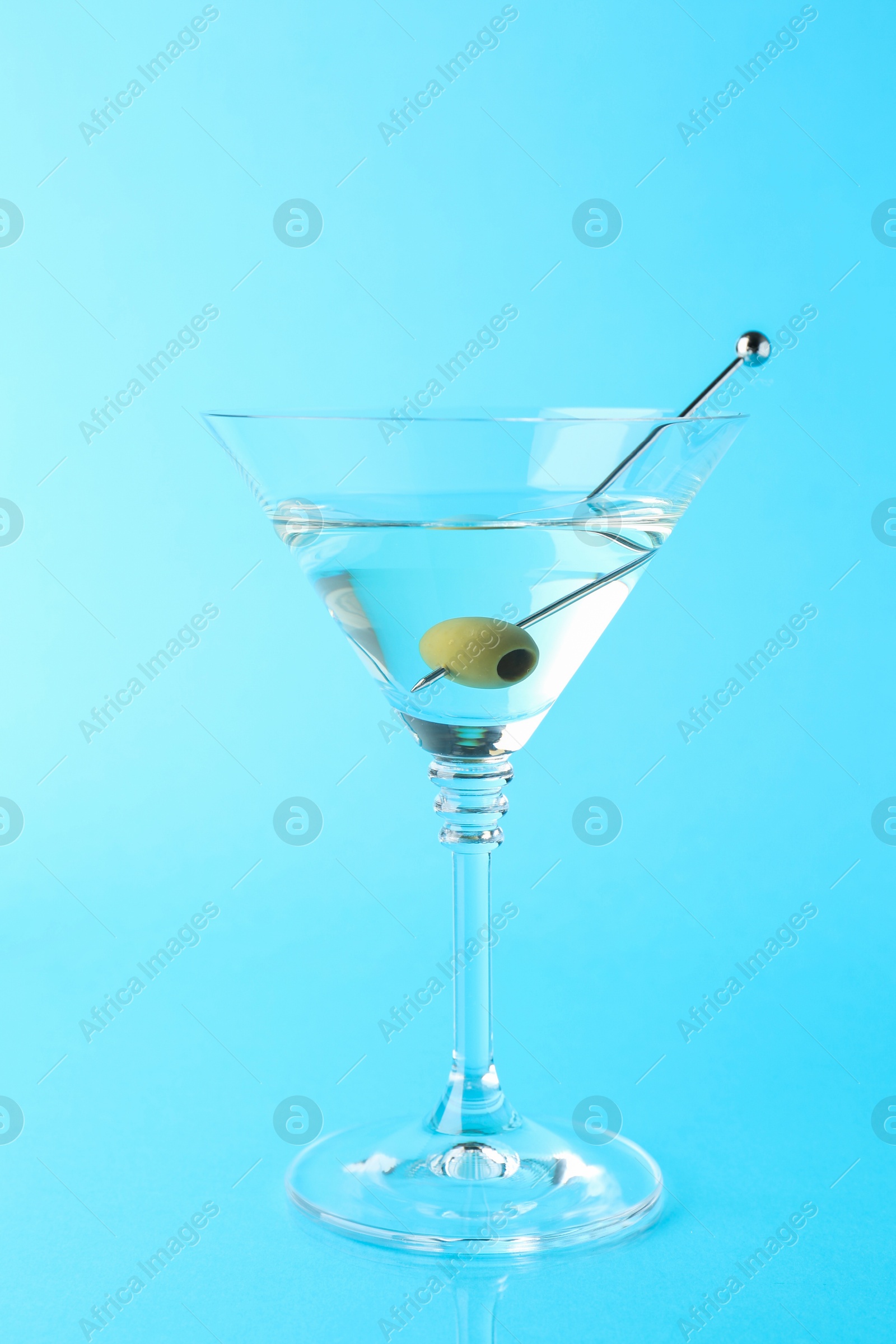 Photo of Martini cocktail with olive in glass on light blue background