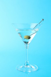 Photo of Martini cocktail with olive in glass on light blue background