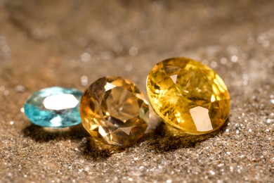 Photo of Beautiful shiny gemstones on sand, closeup view