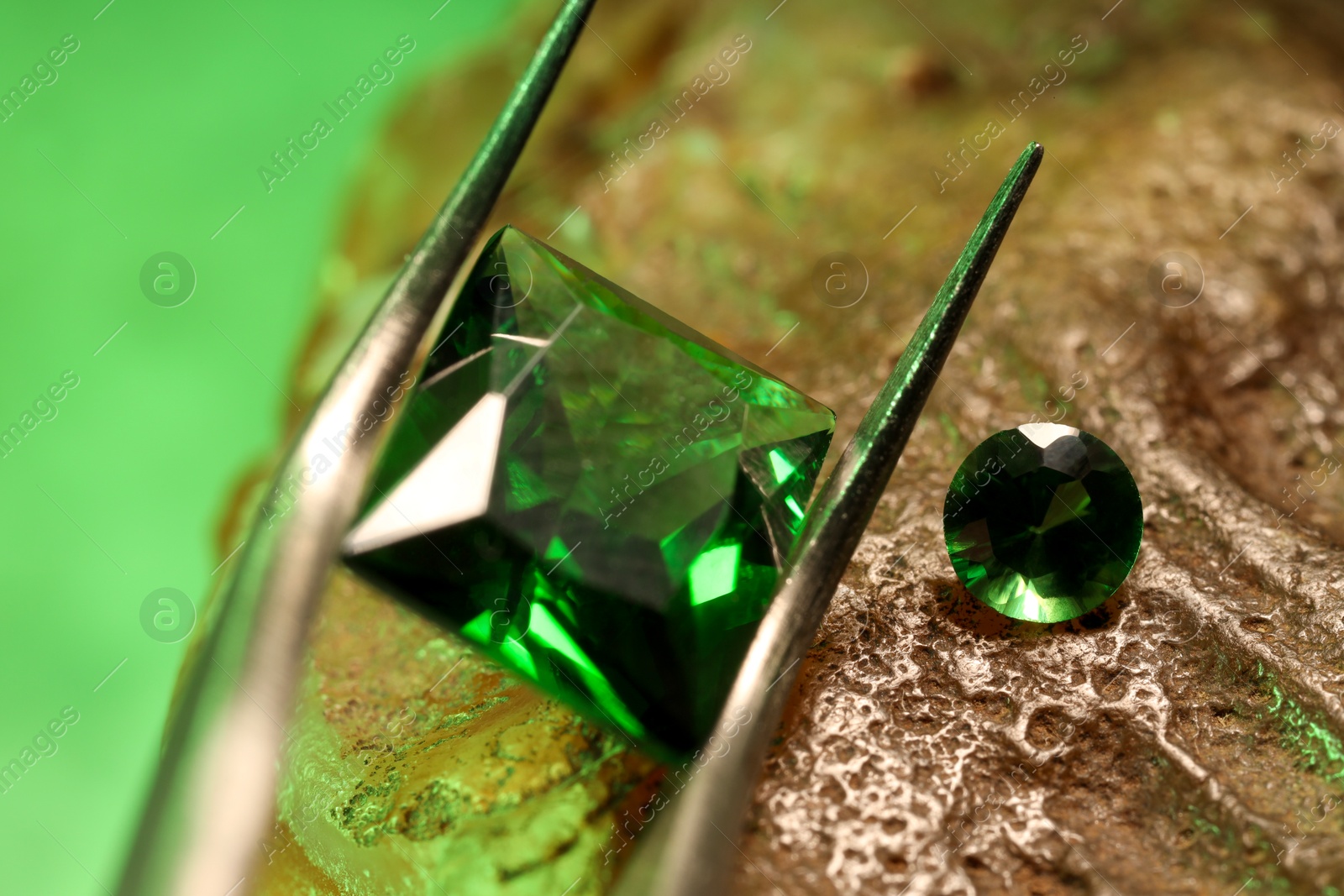 Photo of Tweezers with beautiful green gemstones on stone, closeup