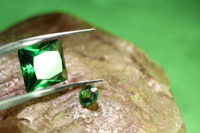 Photo of Tweezers with beautiful green gemstones on stone, closeup. Space for text