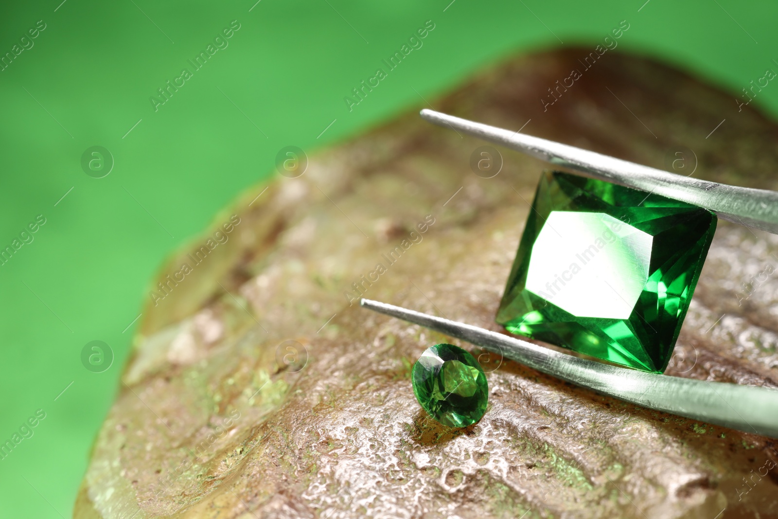 Photo of Tweezers with beautiful green gemstones on stone, closeup. Space for text