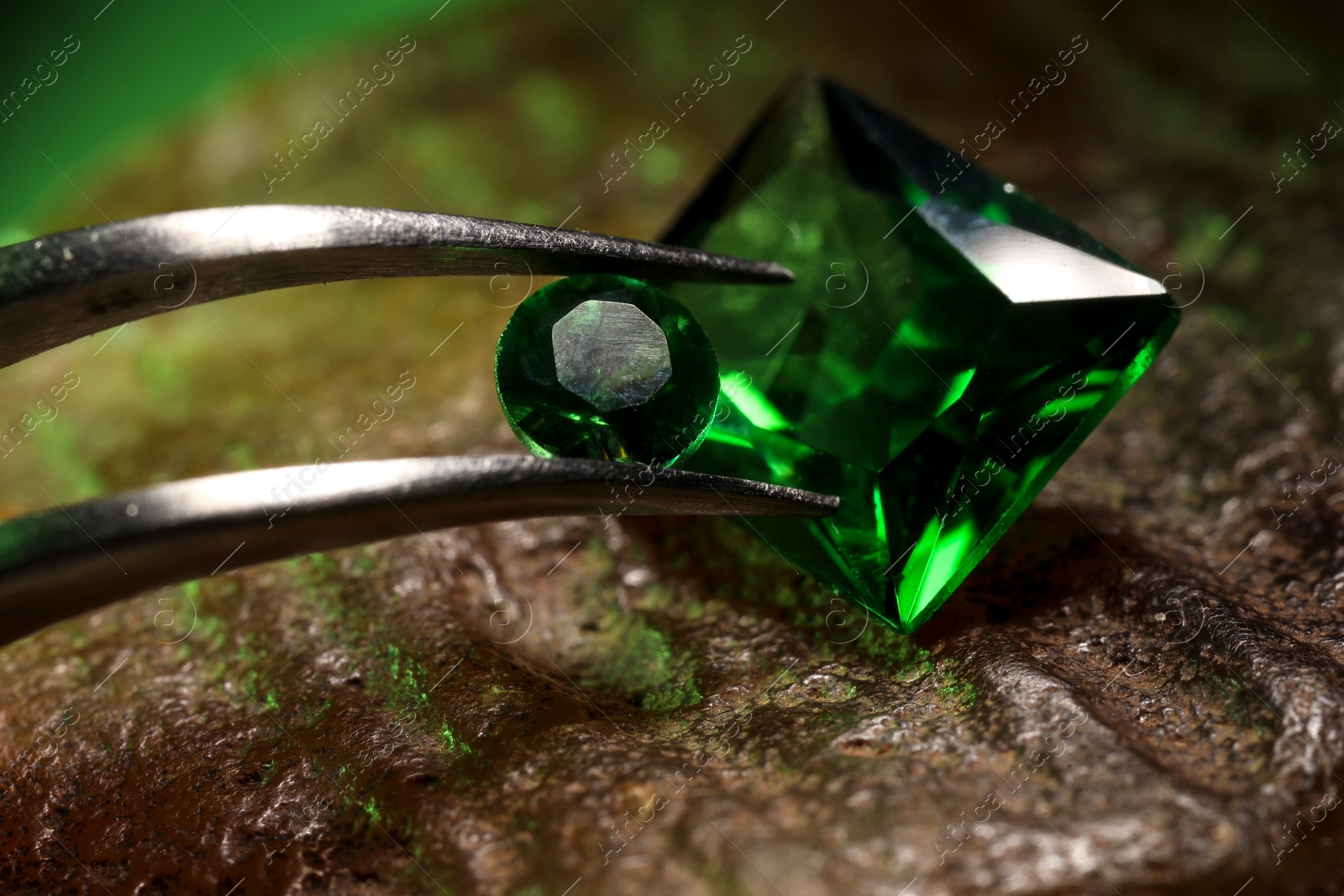 Photo of Tweezers with beautiful green gemstones on stone, closeup