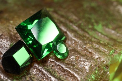 Photo of Beautiful shiny green gemstones on stone, closeup. Space for text