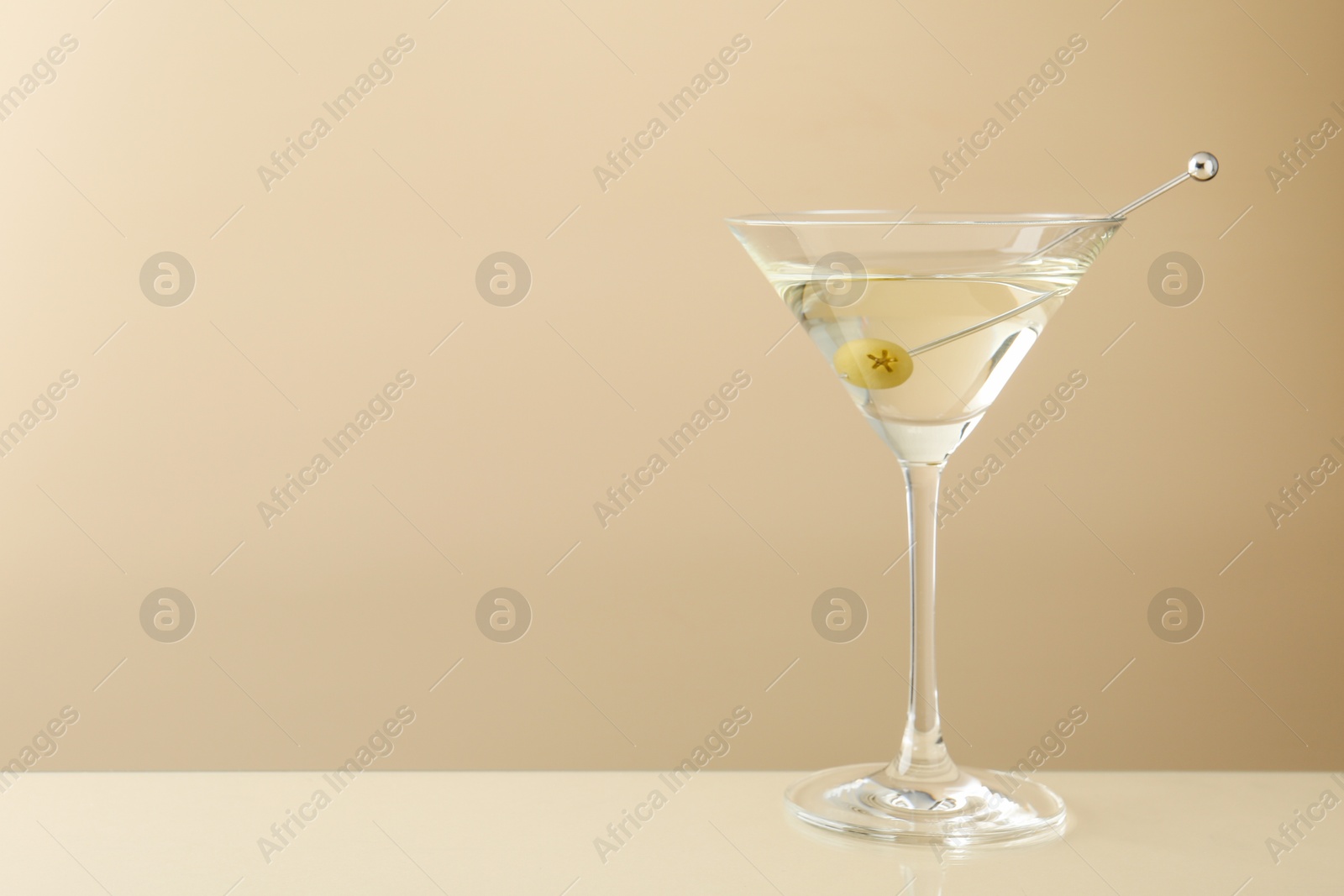 Photo of Martini cocktail with olive in glass on beige table, space for text