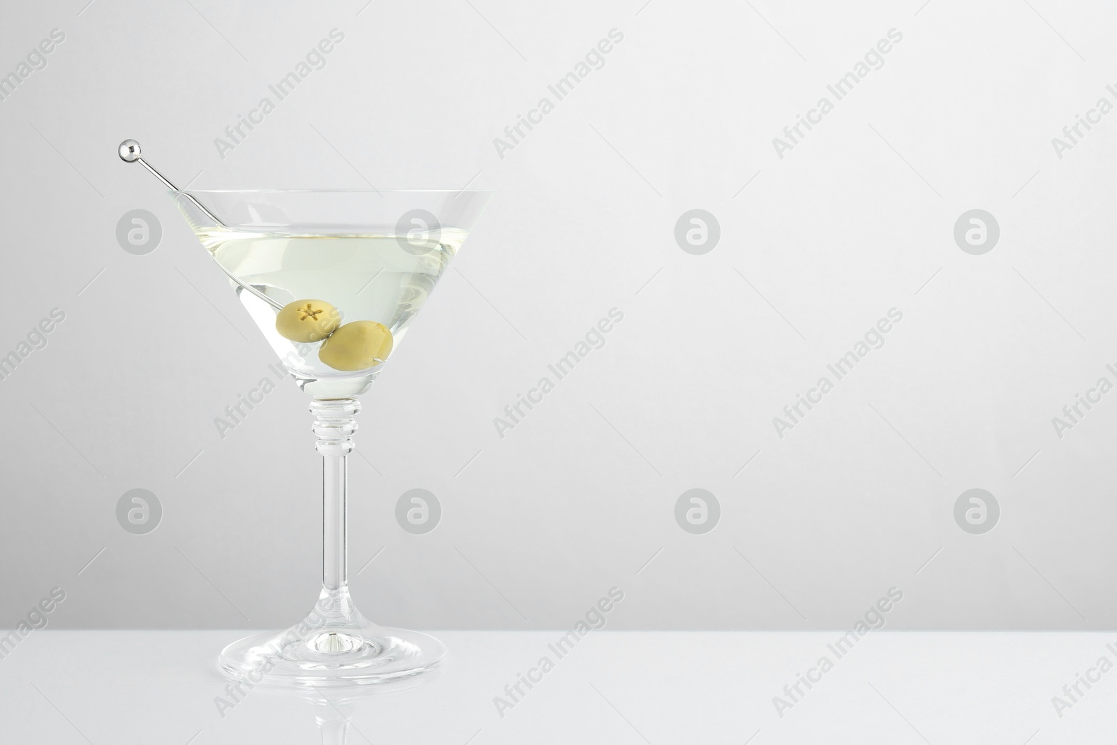 Photo of Martini cocktail with olives in glass on light table, space for text