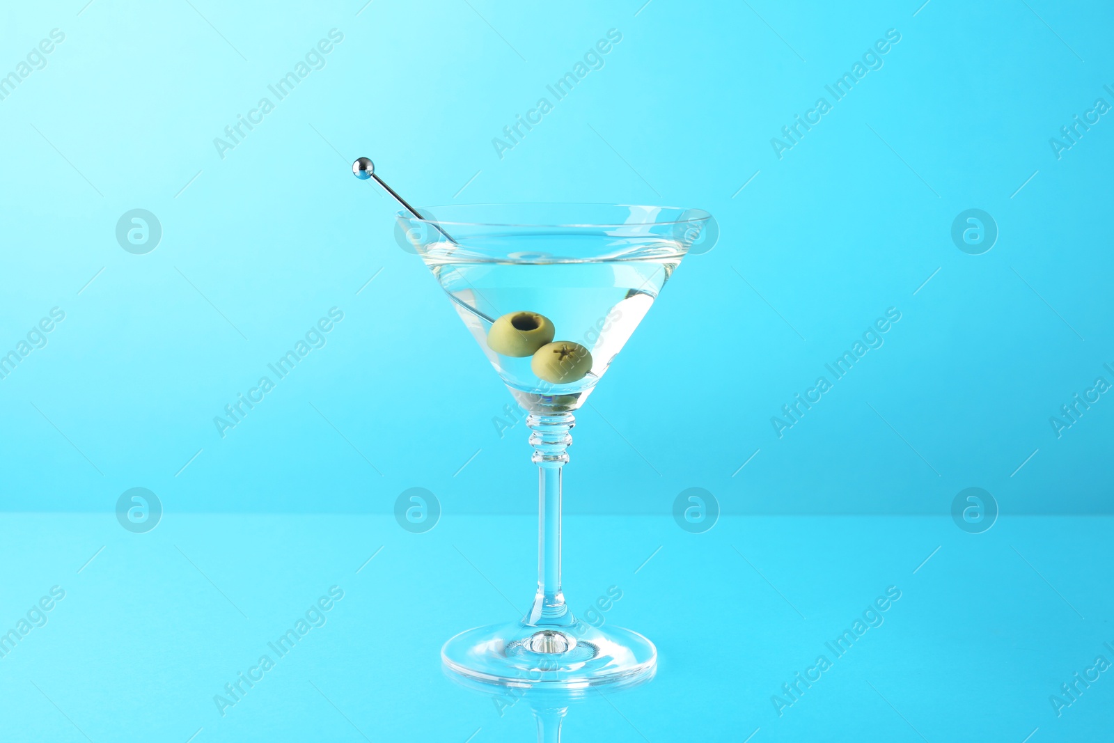 Photo of Martini cocktail with olives in glass on light blue background