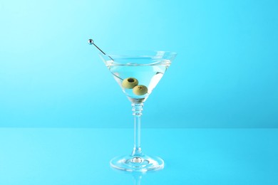 Photo of Martini cocktail with olives in glass on light blue background