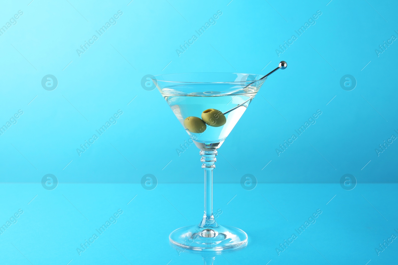 Photo of Martini cocktail with olives in glass on light blue background