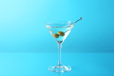 Photo of Martini cocktail with olives in glass on light blue background