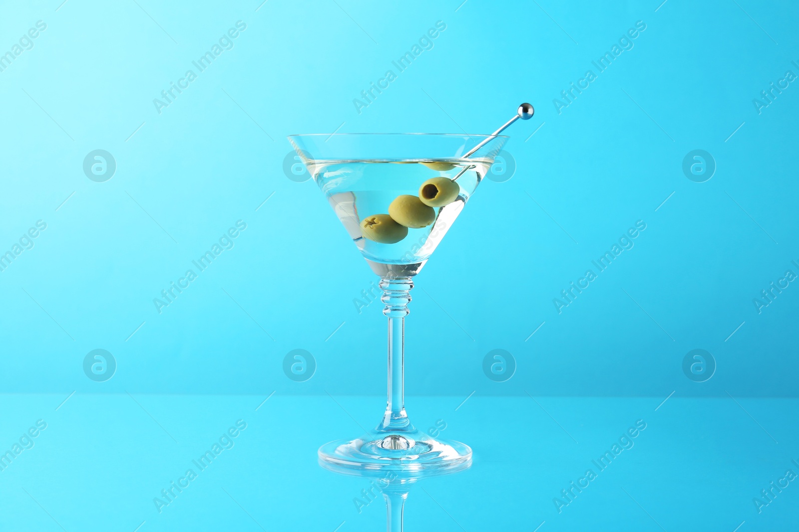 Photo of Martini cocktail with olives in glass on light blue background