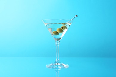 Photo of Martini cocktail with olives in glass on light blue background