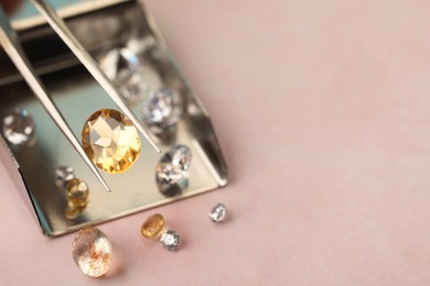 Photo of Tweezers with beautiful gemstones on light pink table, selective focus. Space for text