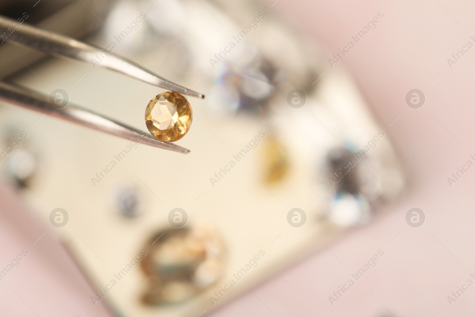 Photo of Tweezers with beautiful gemstone on blurred background, closeup. Space for text