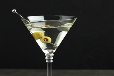 Photo of Martini cocktail with olives in glass on black background, closeup