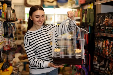 Photo of Smiling woman with bird cage in pet shop