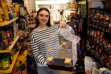 Smiling woman with bird cage in pet shop