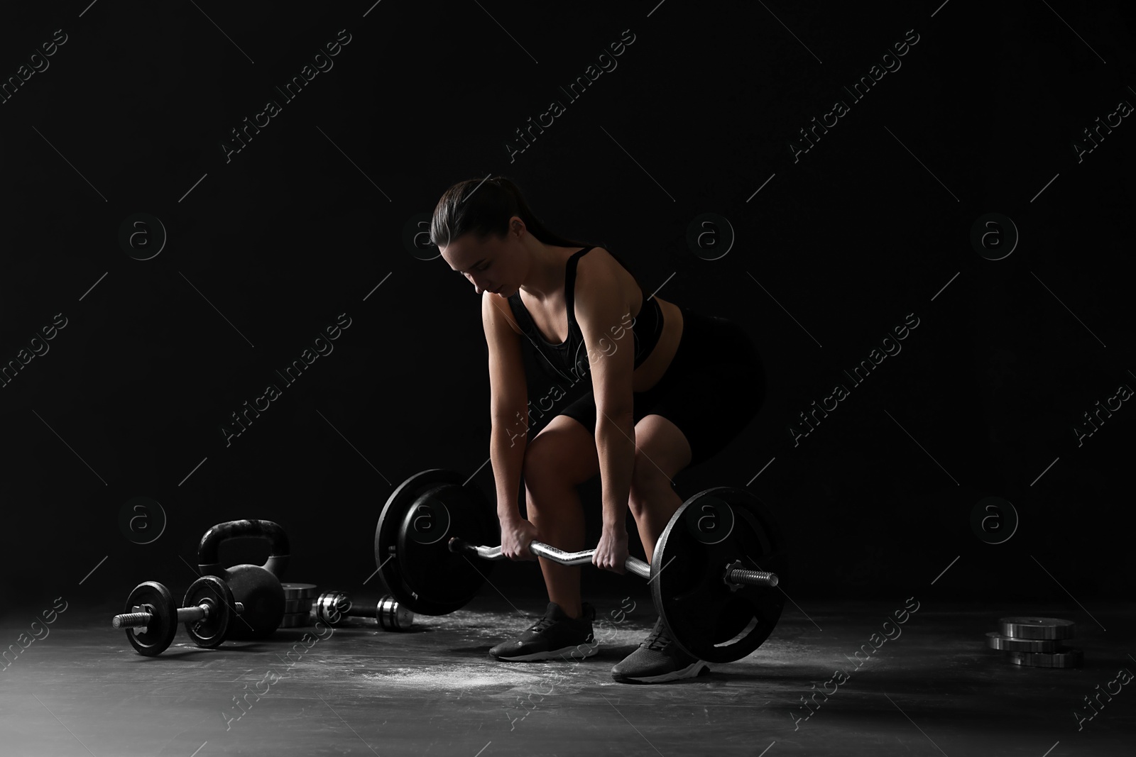 Photo of Woman training with barbell against black background