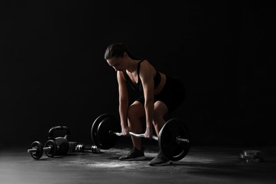 Woman training with barbell against black background