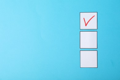 Photo of One checkbox with tick mark among others on light blue background, flat lay. Space for text