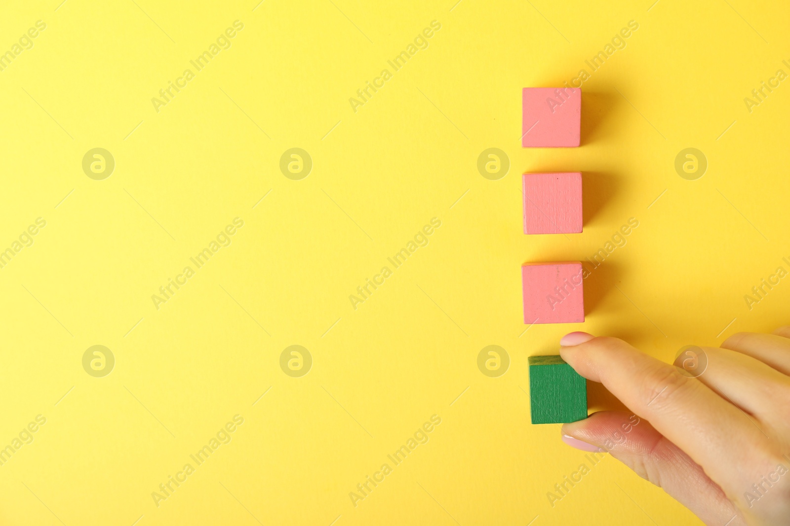 Photo of Woman taking green cube on yellow background, top view. Space for text