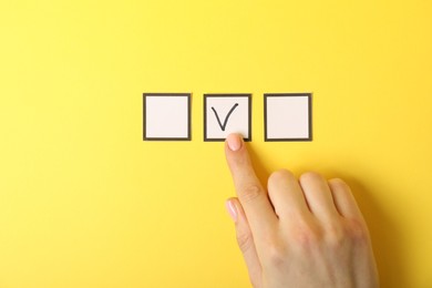 Photo of Woman pointing at checkbox with tick mark on yellow background, top view