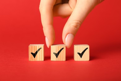 Photo of Woman taking wooden cube with check mark on red background, closeup