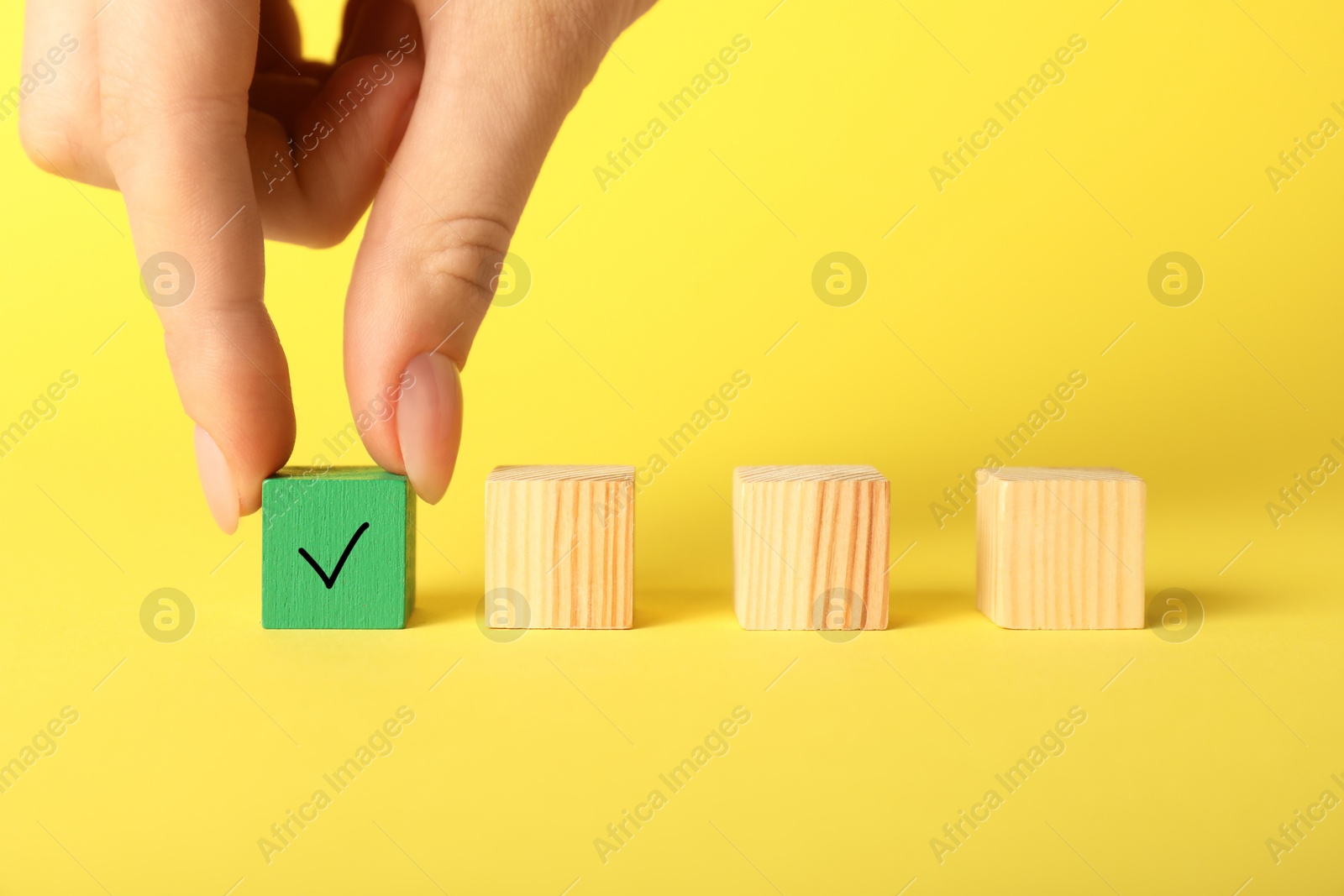 Photo of Woman taking green cube with check mark on yellow background, closeup