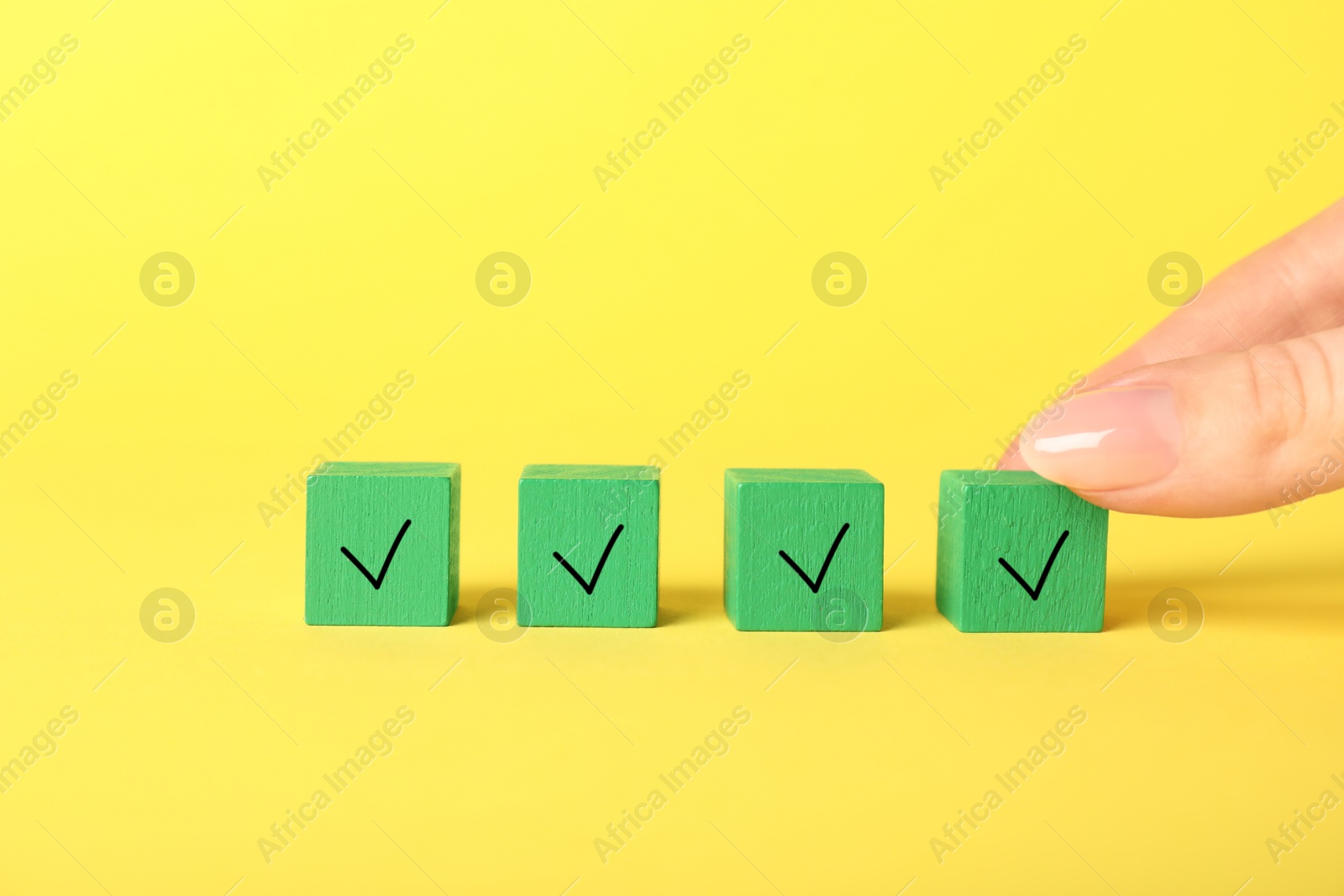 Photo of Woman taking green cube with check mark on yellow background, closeup