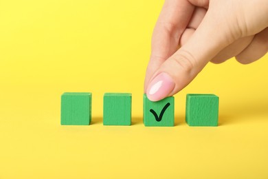 Photo of Woman taking green cube with check mark on yellow background, closeup