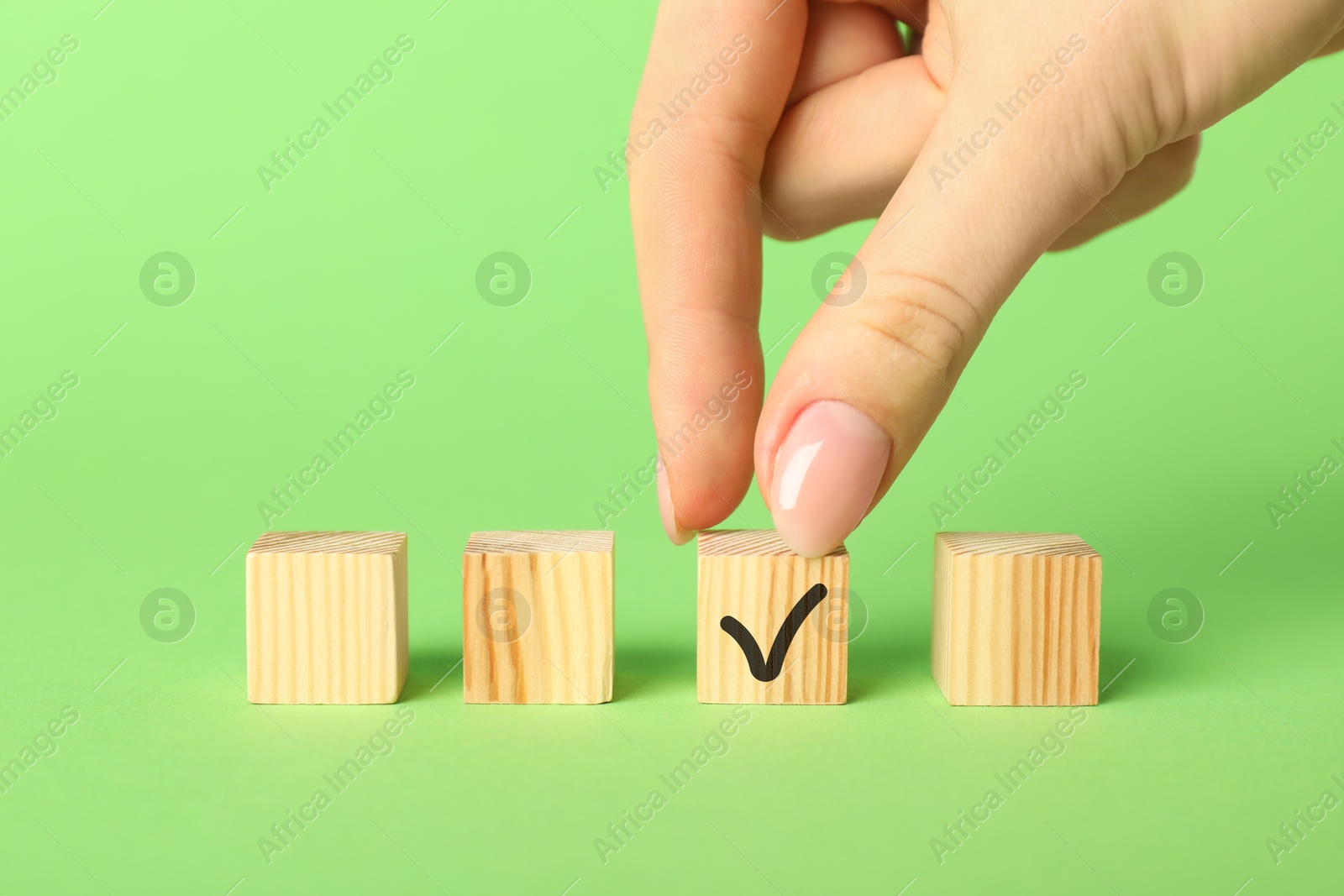 Photo of Woman taking wooden cube with check mark on green background, closeup