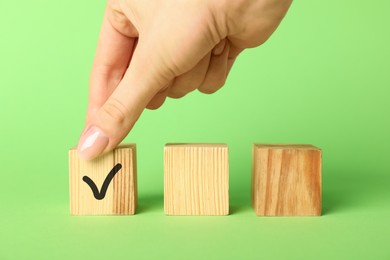 Photo of Woman taking wooden cube with check mark on green background, closeup