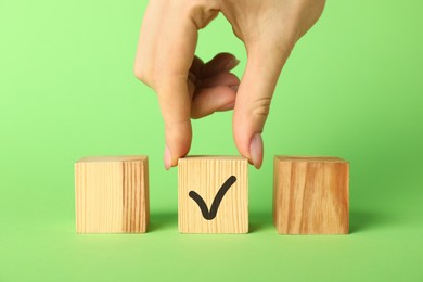 Photo of Woman taking wooden cube with check mark on green background, closeup