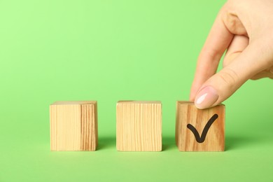 Photo of Woman taking wooden cube with check mark on green background, closeup