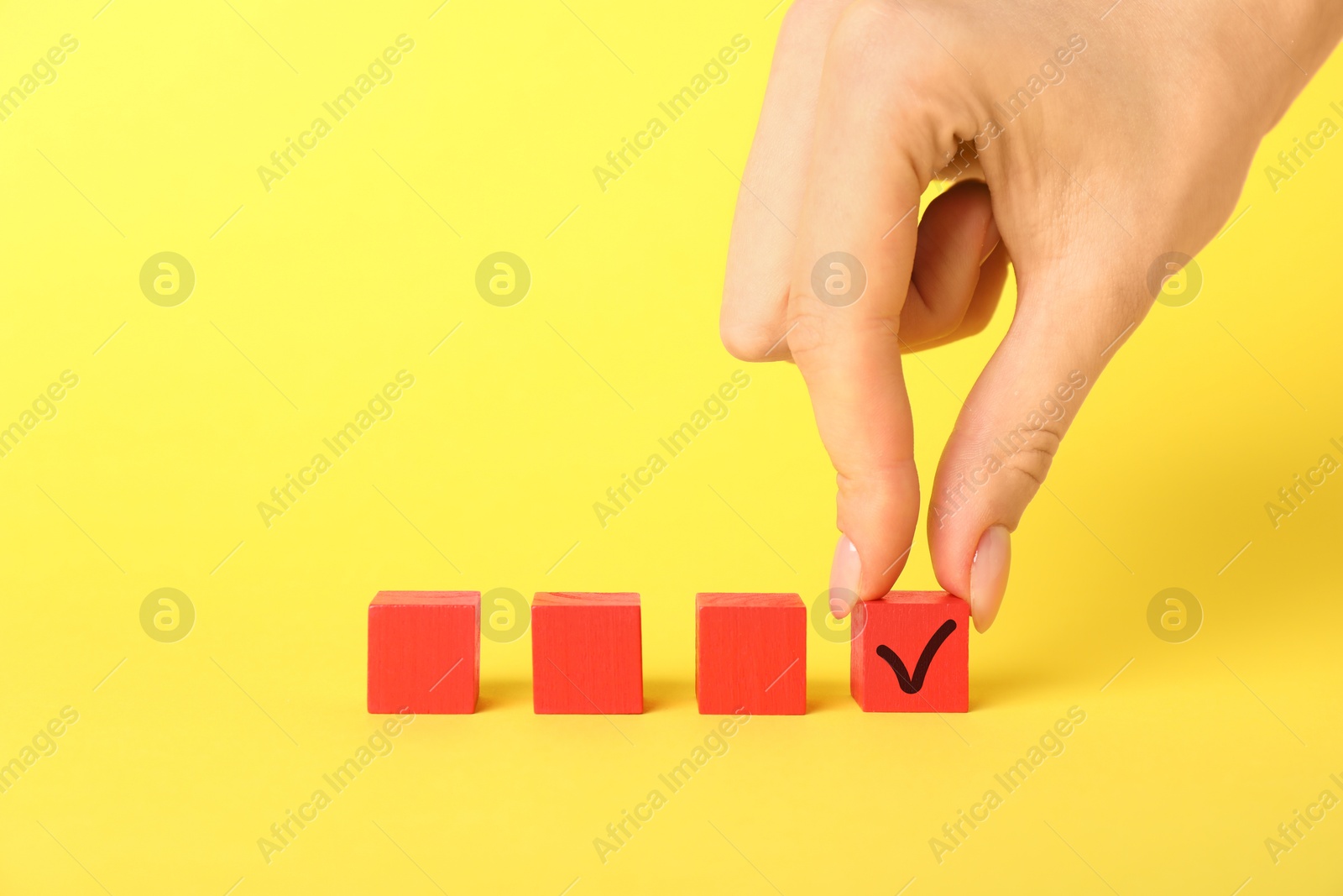 Photo of Woman taking red cube with check mark on yellow background, closeup