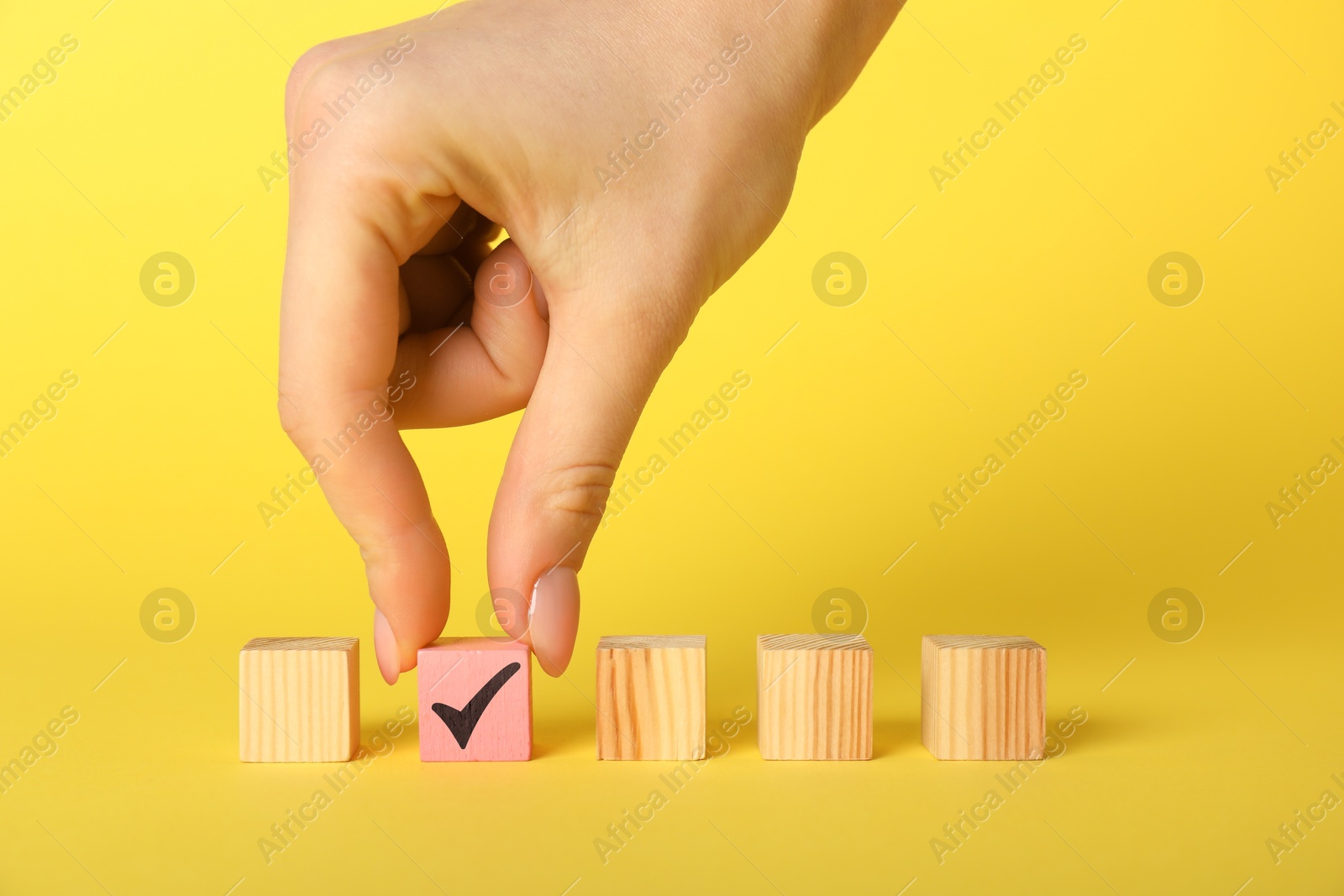 Photo of Woman taking pink cube with check mark on yellow background, closeup