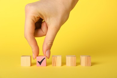 Photo of Woman taking pink cube with check mark on yellow background, closeup