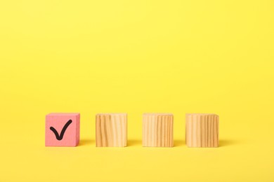 Photo of One pink cube with check mark among others on yellow background