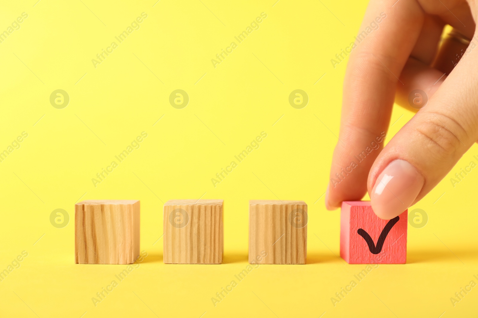 Photo of Woman taking pink cube with check mark on yellow background, closeup