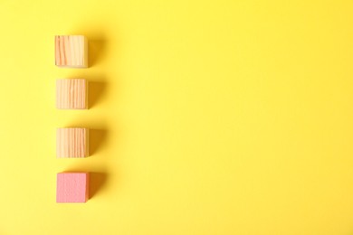 Photo of Many wooden cubes and pink one on yellow background, flat lay. Space for text