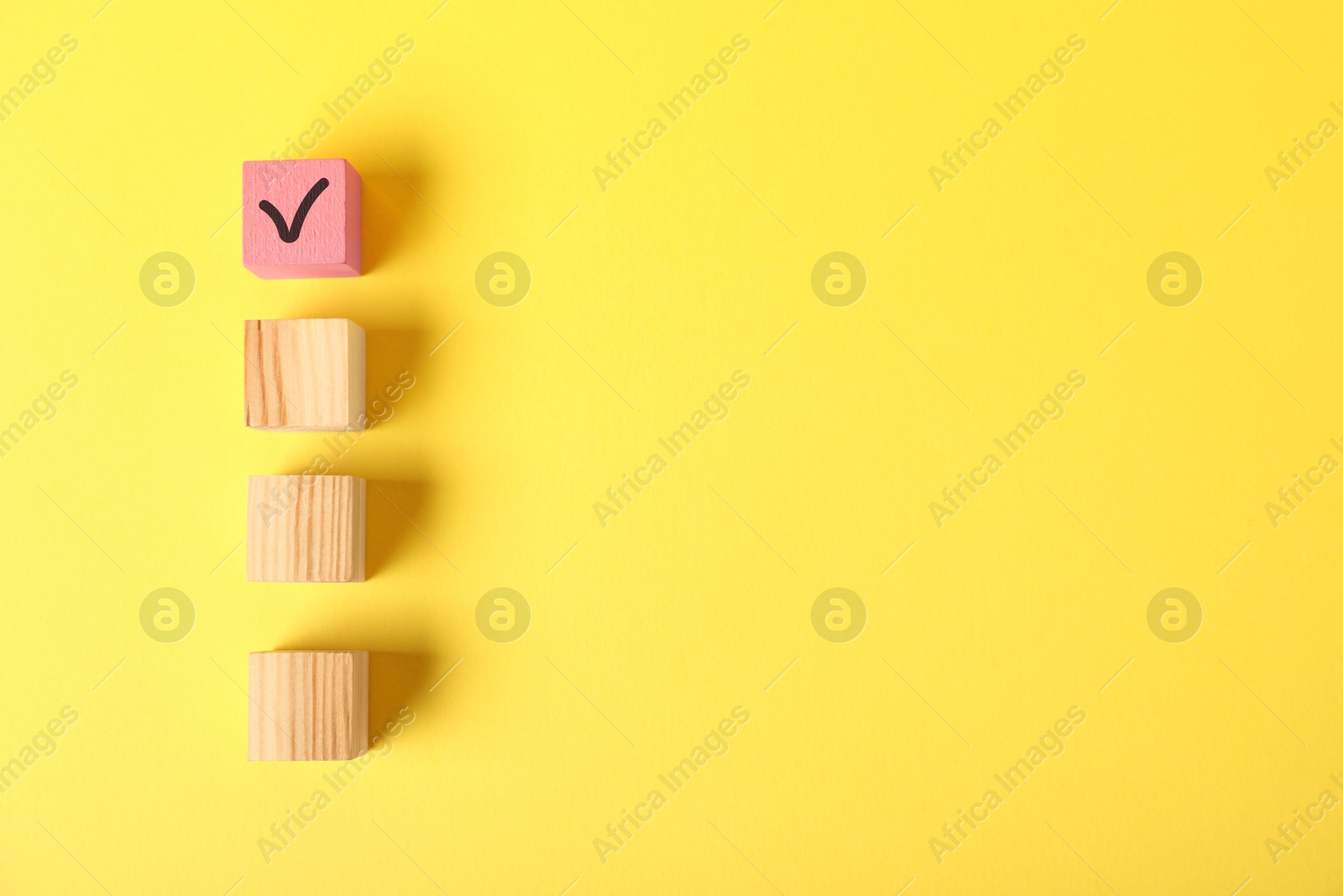 Photo of One pink cube with check mark among others on yellow background, flat lay. Space for text